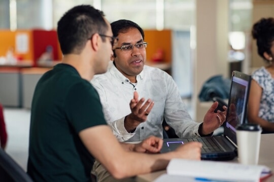 Two men collaborating and discussing in front of laptop