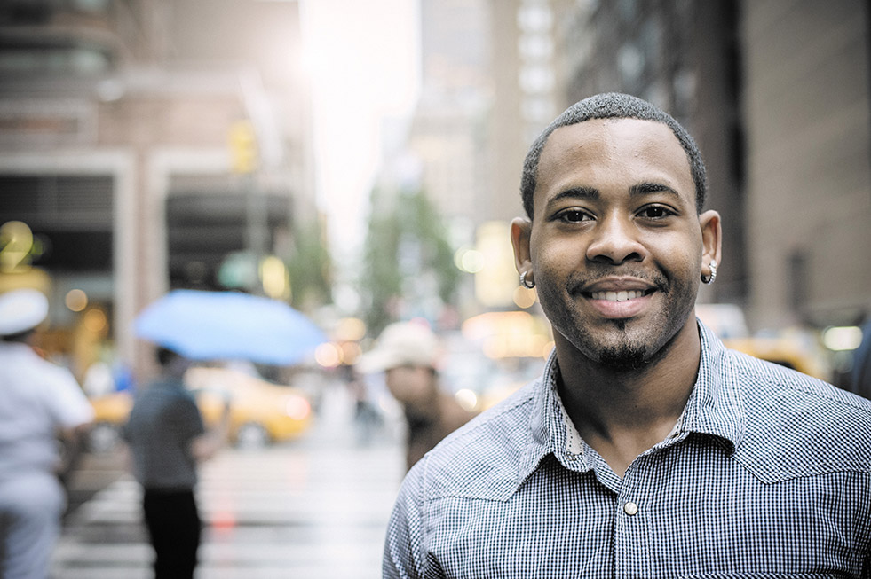 A young black professional man smiles at the camera on the street with umbrellas in the background