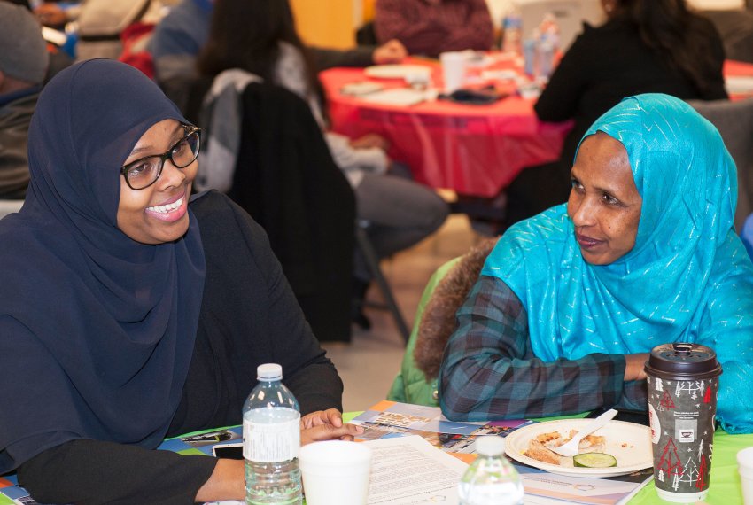 A young woman in hijab smiles at an event while sitting at a table