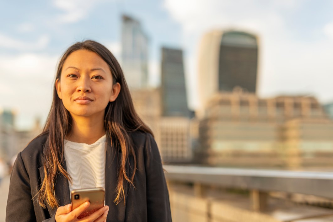 A young student with city in the background holds her phone