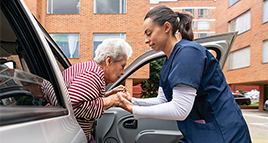 A nurse helps an older woman out of a car