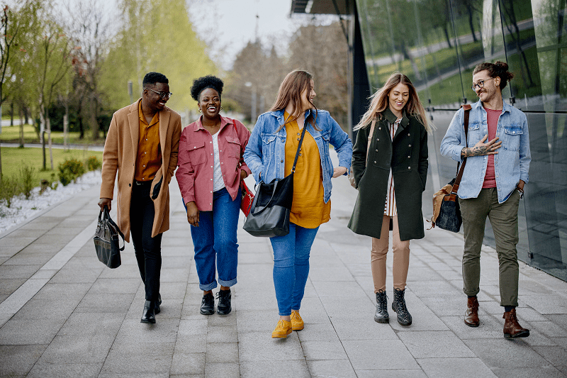 Group of five young professionals smiling and walking on the street